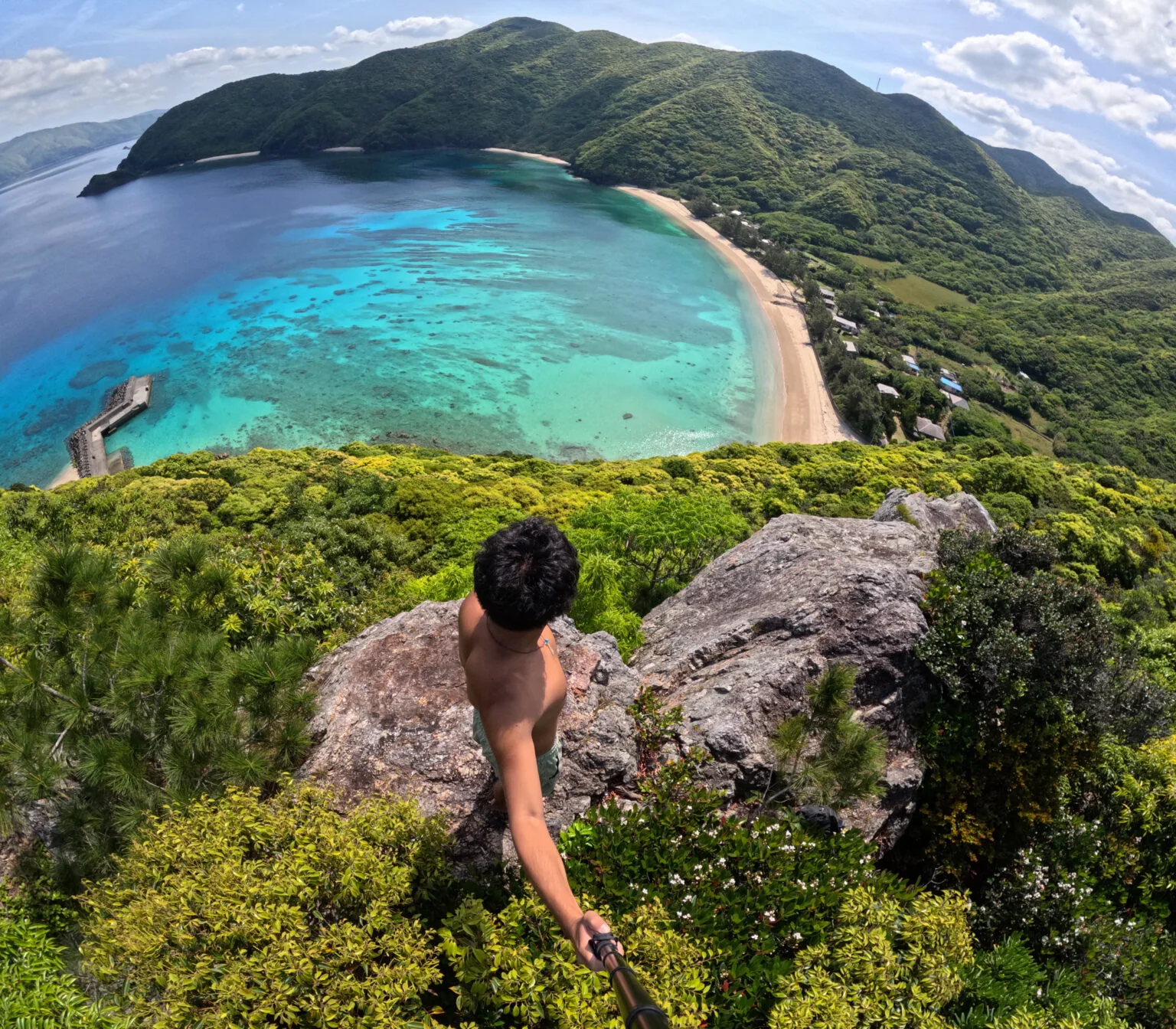 加計呂麻島の湾を見下ろす岩の上で撮影するガイドのようへい